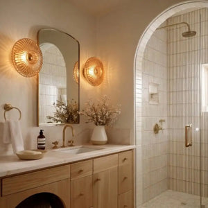 Arandela de Parede de Vidro Corrugado Fumê Conhaque com acabamento dourado iluminando bancada de banheiro moderno com paredes claras e design sofisticado.