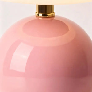 Close-up detalhado da base esférica de cerâmica rosa, destacando o acabamento brilhante e o conector dourado. Realça a qualidade premium do abajur