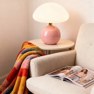 Abajur rosa em um cantinho de leitura, sobre uma mesa de apoio, com uma poltrona e uma manta colorida. A luminária de mesa de design adiciona alegria ao ambiente