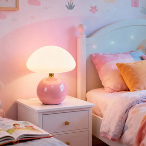 Abajur rosa de cerâmica em um quarto infantil, sobre uma mesa de cabeceira branca. A luminária cogumelo cria um ambiente divertido e aconchegante