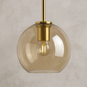 Detalhe do pendente globo âmbar dourado com vidro soprado translúcido e lâmpada LED em soquete dourado refinado.