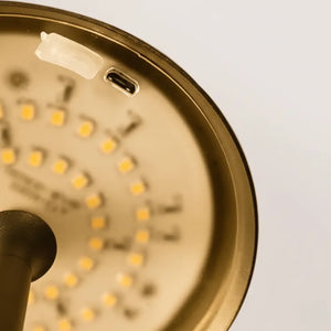 Vista em close-up da parte interna da luminária de mesa dourada, mostrando o arranjo de LEDs e a porta de carregamento USB. Otimizada para durabilidade e alta performance