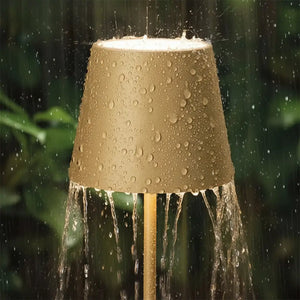 Luminária de mesa dourada sendo usada em um ambiente externo sob chuva leve, demonstrando sua resistência à água e durabilidade