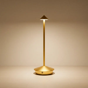 Luminária de mesa portátil dourada com acabamento em latão escovado, sobre uma superfície clara e luxuosa. Perfeita para um design de interiores sofisticado.