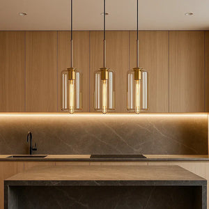 Pendente cilíndrico de vidro âmbar em conjunto de três peças sobre bancada de cozinha planejada