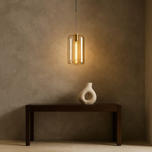 Luminária pendente cilíndrica âmbar dourada destacando parede de cimento queimado com mesa de apoio