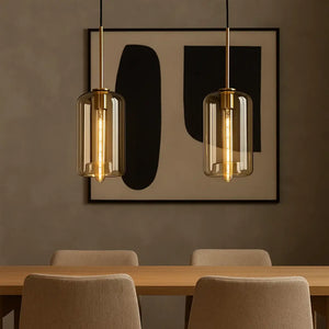 Duas luminárias pendentes cilíndricas de vidro âmbar dourado iluminando ambiente sofisticado