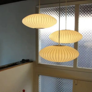 Composição com três luminárias pendentes japonesas ovais em seda instaladas em alturas diferentes em um vão de escada com janela de vidro fosco.