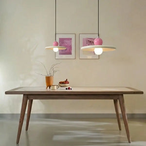 Composição de iluminação com dois lustres pendentes estilo francês minimalista na cor rosa, tamanhos 20cm e 30cm, acesos sobre uma mesa de jantar contemporânea