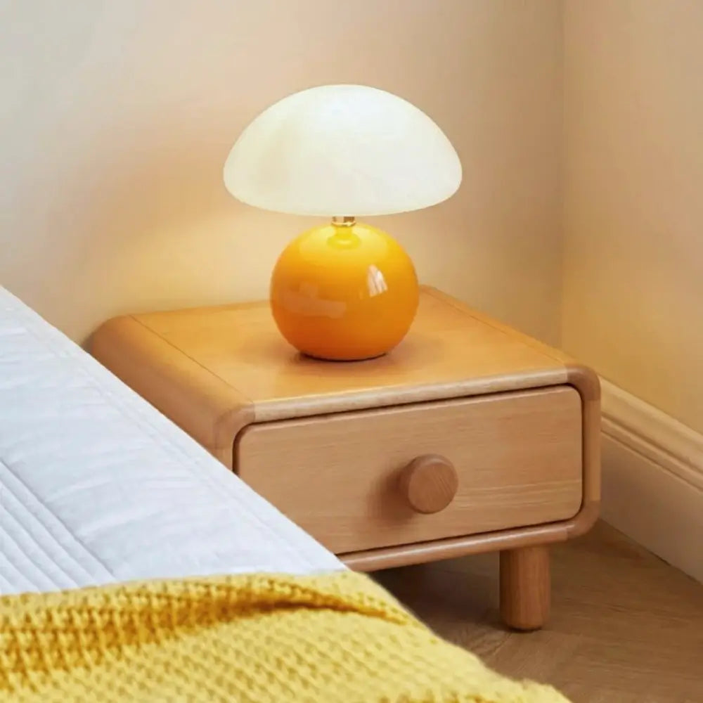 Abajur Cogumelo Laranja aceso sobre mesa de cabeceira de madeira em quarto de casal. Iluminação de luz quente (3000K) ideal para leitura e ambiente aconchegante.