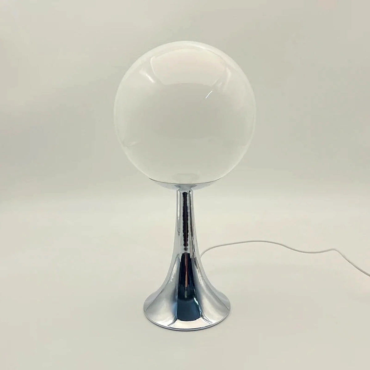 Abajur Globo Eira em fundo neutro com base cromada e cabo branco