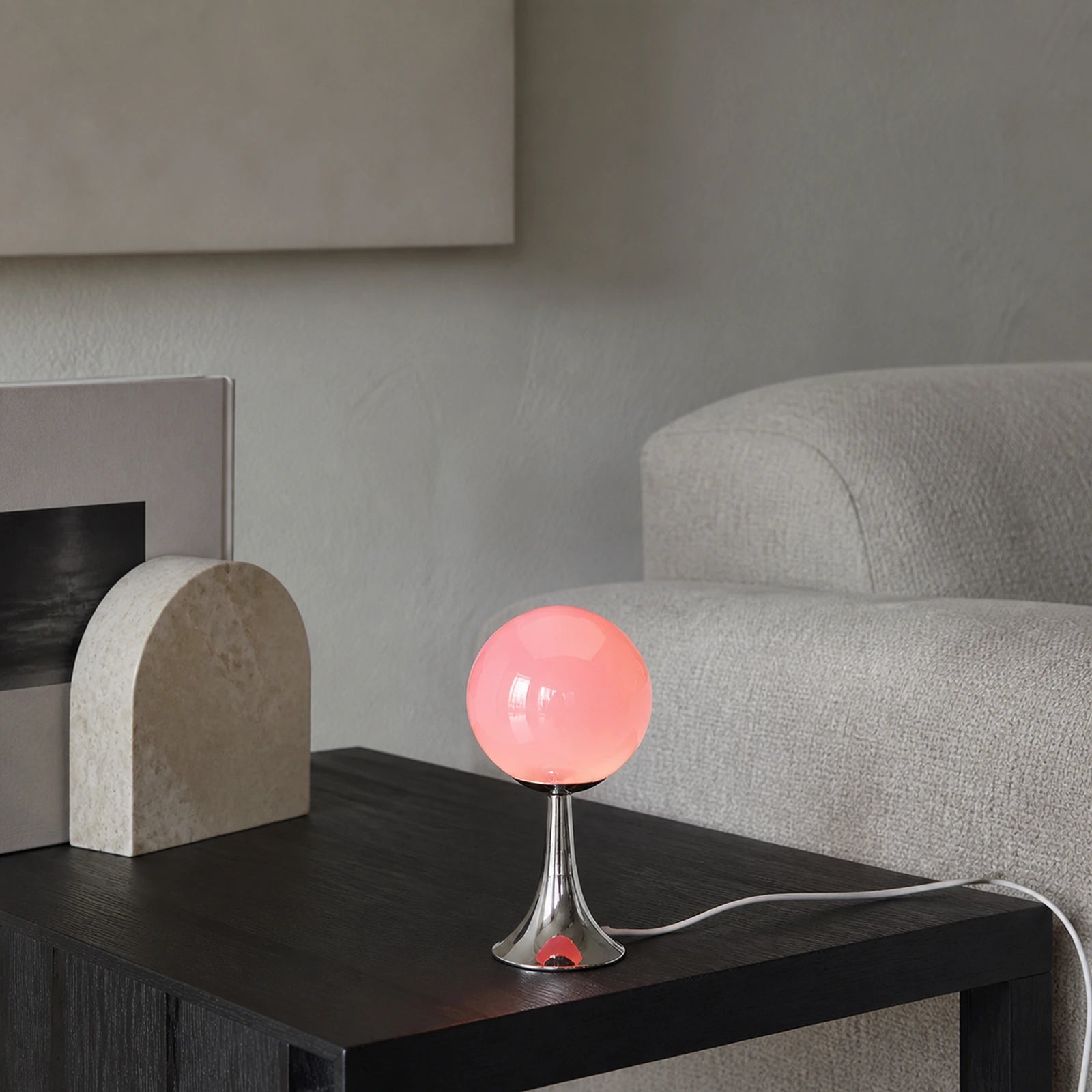 Abajur Globo Mika em sala com luz neutra, mesa escura e cabo branco visível