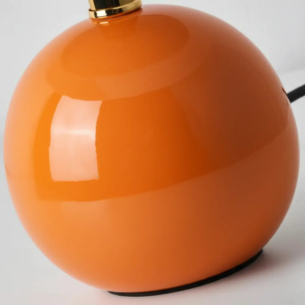 Close-up da base esférica de cerâmica brilhante do abajur laranja cogumelo, evidenciando o acabamento de alta qualidade e o design moderno. Destaca a cor e a textura do material