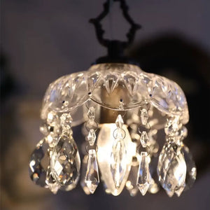 Close-up da luminária pendente de vidro facetado tipo cristal Marquise Radiantbr acesa, destacando os reflexos da luz quente nos pingentes em gota contra um fundo escuro.