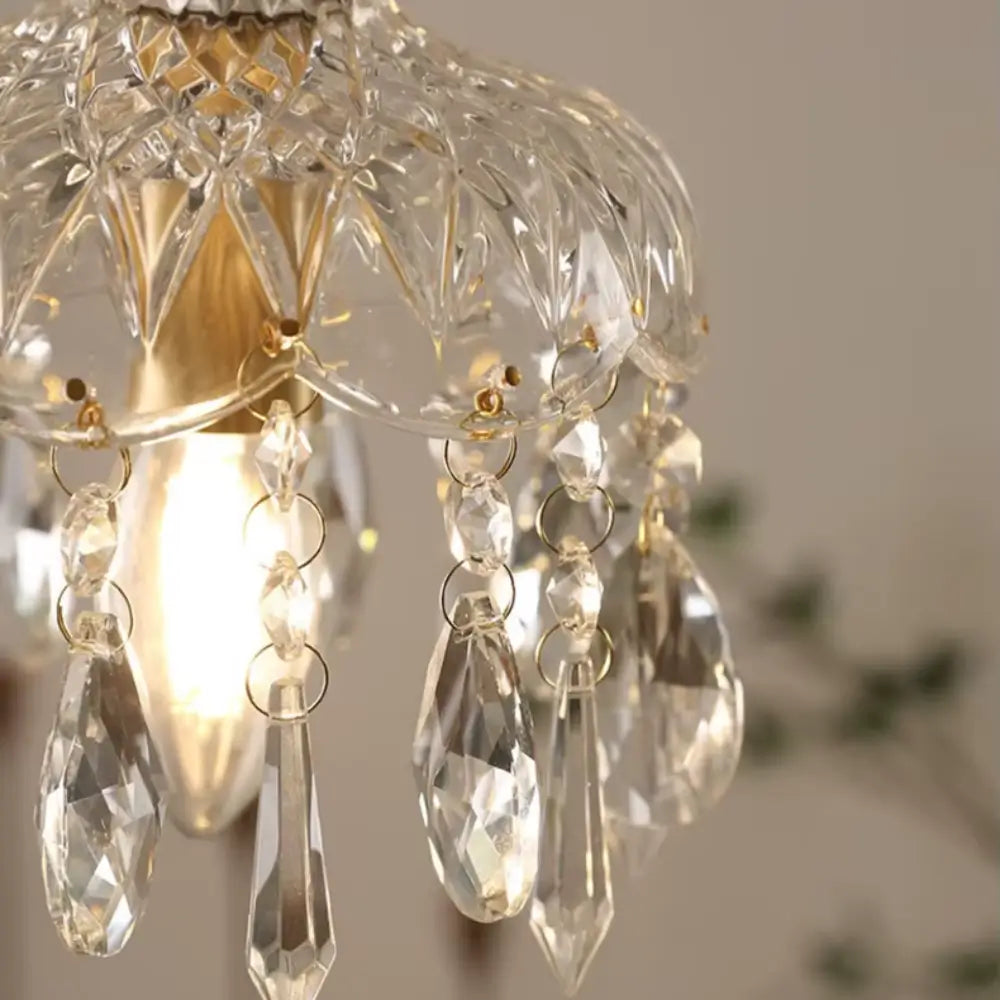 Close-up dos pingentes de cristal e do vidro facetado da luminária pendente Marquise, mostrando o detalhe das argolas douradas e a lâmpada quente acesa.