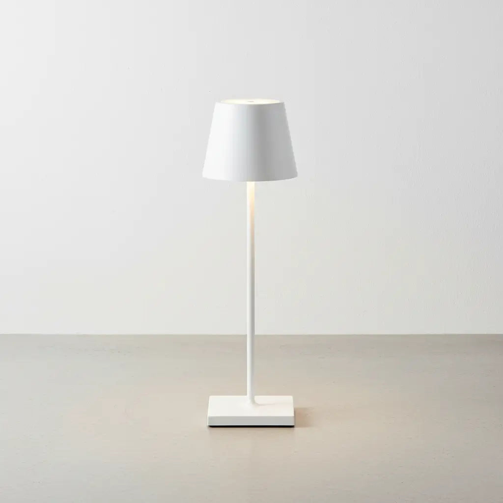 Luminária de mesa branca de design, com luz suave acesa, sobre um piso de concreto claro. Design clássico e moderno para ambientes minimalistas