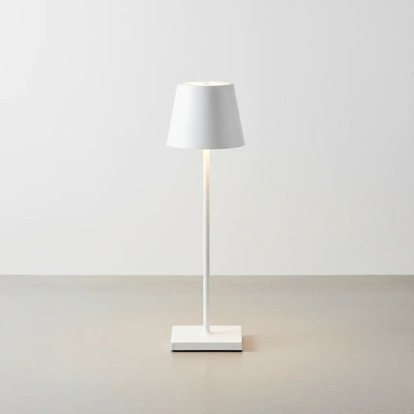 Luminária de mesa branca de design, com luz suave acesa, sobre um piso de concreto claro. Design clássico e moderno para ambientes minimalistas