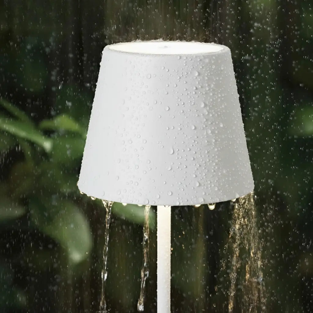 Luminária de mesa branca sendo usada em ambiente externo, com gotas de água escorrendo sobre a cúpula, mostrando sua durabilidade e resistência à água.