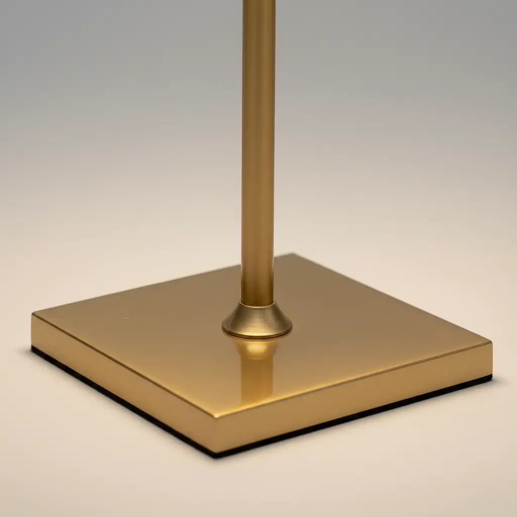 Close-up detalhado da base quadrada da luminária de mesa dourada, destacando o acabamento polido e o design de alta qualidade