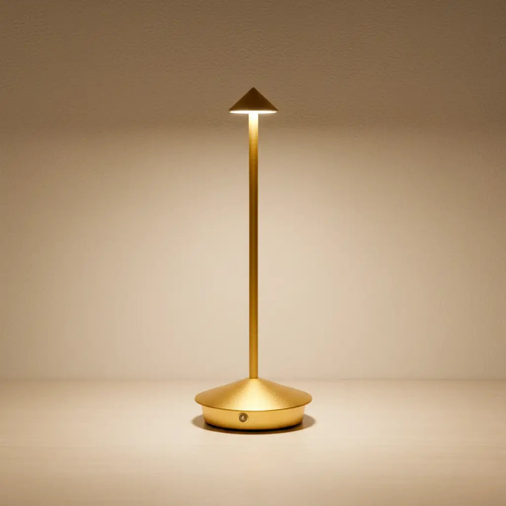 Luminária de mesa portátil dourada com acabamento em latão escovado, sobre uma superfície clara e luxuosa. Perfeita para um design de interiores sofisticado.


