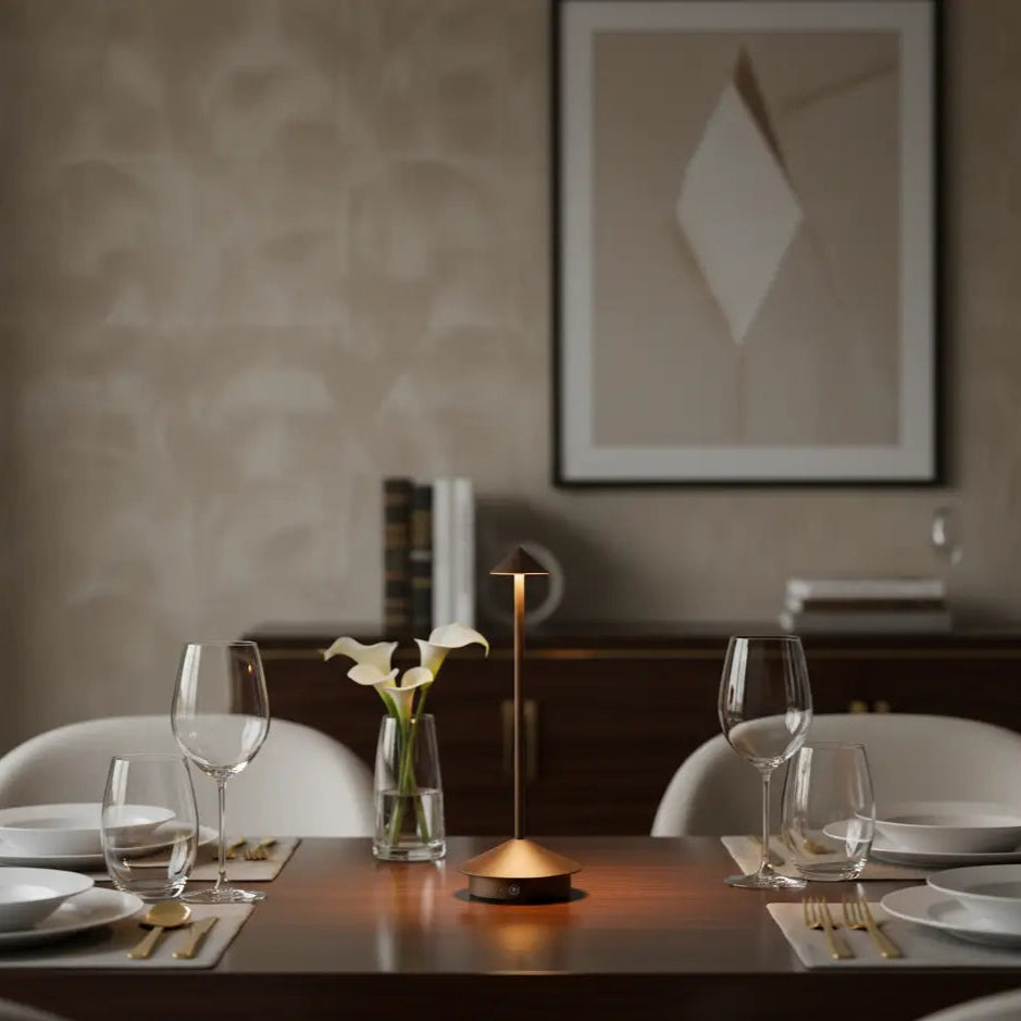 Luminária de mesa sem fio com design minimalista, usada para iluminar uma mesa de jantar de madeira escura com taças de vinho e louças, criando uma atmosfera aconchegante