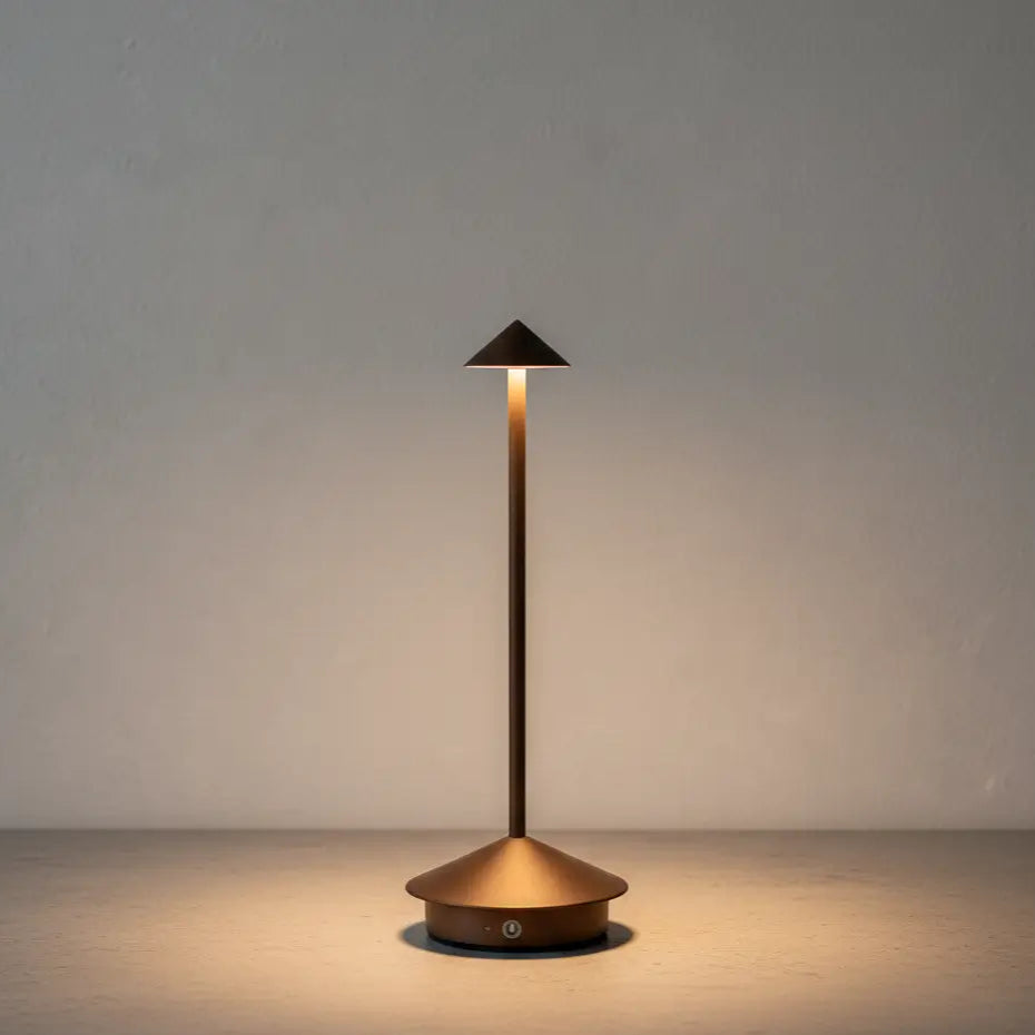 Luminária de mesa portátil sem fio na cor marrom, com luz LED acesa, sobre uma base de concreto texturizada