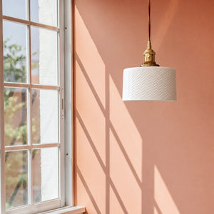 Luminária Pendente Ori com cúpula branca texturizada próxima à janela e parede terracota