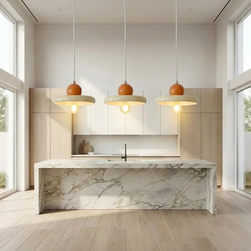 Trio de luminárias pendentes modernas minimalistas com esfera retrô laranja e disco creme. Instaladas harmoniosamente sobre uma ilha de mármore, sendo a escolha ideal de lustre na cozinha ou pendente para bancada colorida.