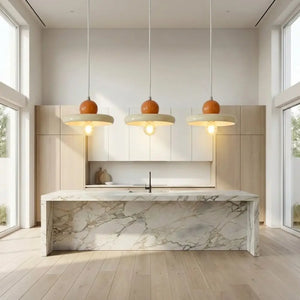 Trio de luminárias pendentes modernas minimalistas com esfera retrô laranja e disco creme. Instaladas harmoniosamente sobre uma ilha de mármore, sendo a escolha ideal de lustre na cozinha ou pendente para bancada colorida.