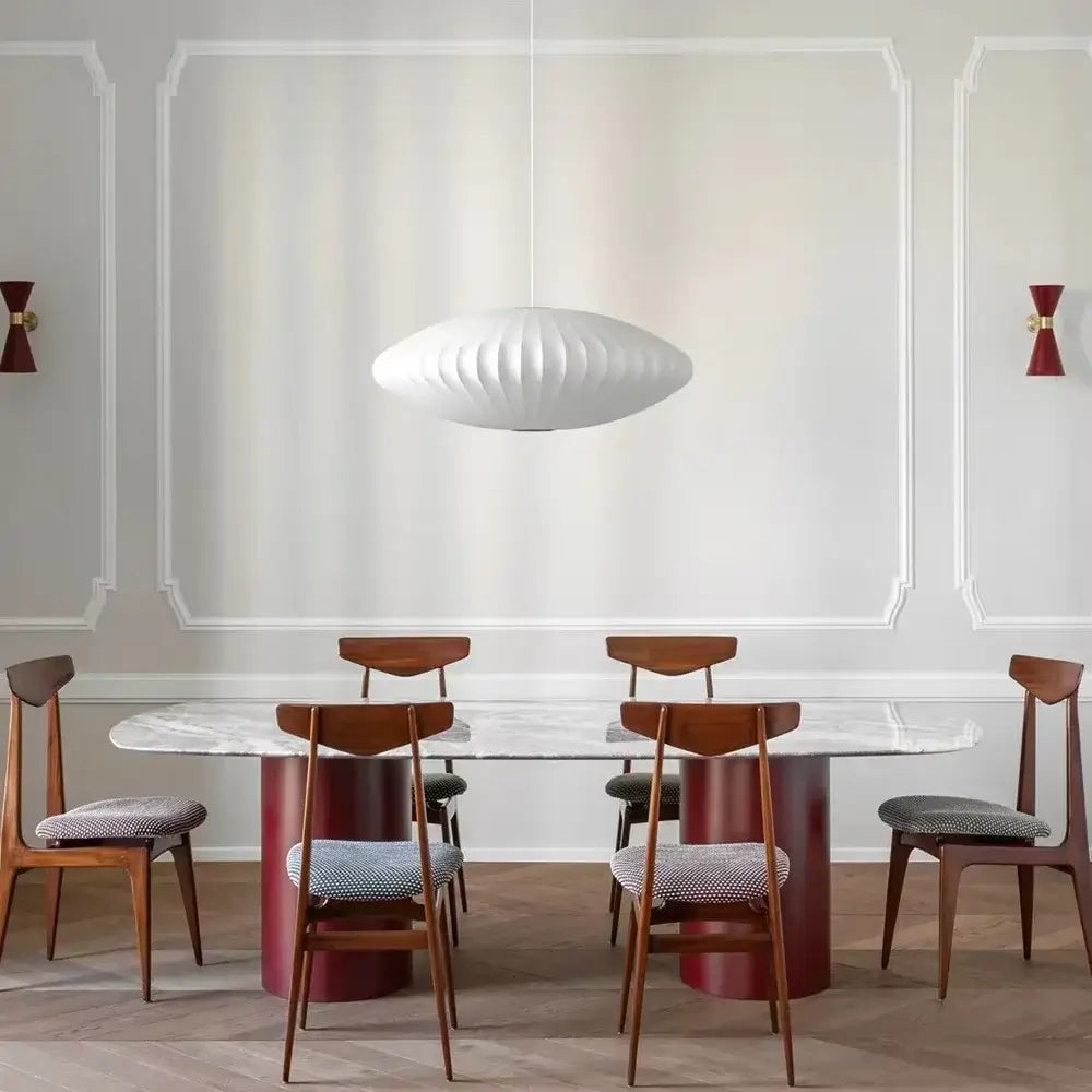 Luminária pendente japonesa oval em seda branca iluminando uma mesa de jantar de mármore retangular em uma sala de estilo moderno com paredes molduradas e arandelas vermelhas.