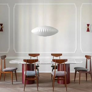 Luminária pendente japonesa oval em seda branca iluminando uma mesa de jantar de mármore retangular em uma sala de estilo moderno com paredes molduradas e arandelas vermelhas.