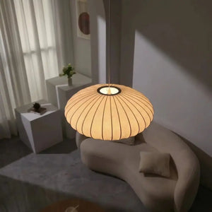 Luminária pendente japonesa oval em seda com iluminação quente suspensa sobre um sofá curvo bege em uma sala de estar minimalista e aconchegante.