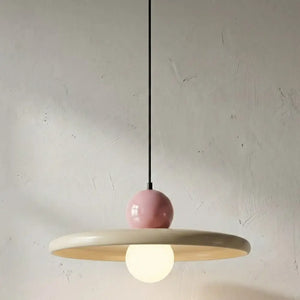Luminária pendente moderna minimalista acesa, destacando a cúpula em metal creme e a esfera superior rosa com design retrô. Uma excelente opção de lustre colorido e elegante para sala de jantar ou quarto.