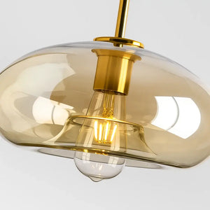 Detalhe da Luminária Pendente de Vidro Âmbar com estrutura dourada e lâmpada acesa, iluminação sofisticada Radiantbr