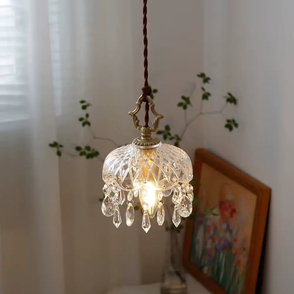 Luminária pendente de vidro facetado tipo cristal Marquise Radiantbr acesa com luz quente, compondo a decoração de um ambiente aconchegante com planta e quadro ao fundo.