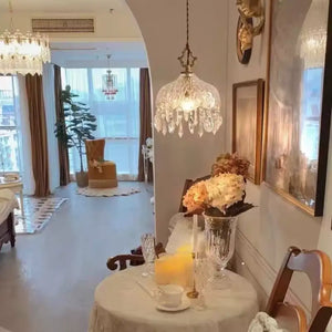 Luminária pendente de vidro facetado tipo cristal Marquise Radiantbr pendurada sobre mesa lateral de madeira em quarto decorado com estante de livros