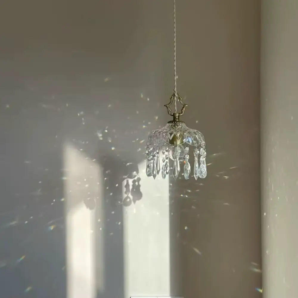 Luminária pendente de vidro facetado tipo cristal Marquise Radiantbr apagada, recebendo luz solar direta que projeta sombras e reflexos prismáticos na parede clara.