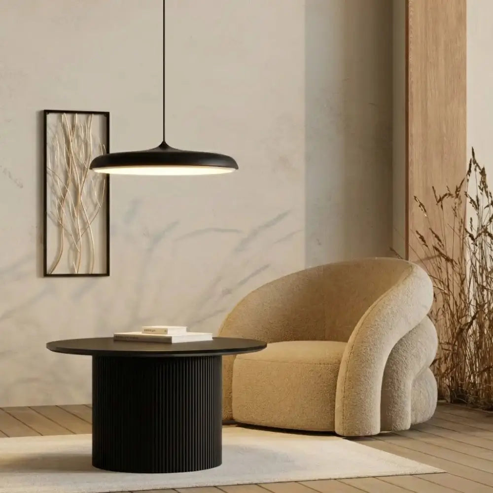 Decoração de sala de estar estilo Japandi com Pendente Macaron Preto suspenso baixo sobre mesa lateral, criando um canto de leitura aconchegante junto à poltrona.