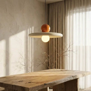 Luminária pendente moderna minimalista com esfera retrô laranja e disco creme, instalada de forma elegante como lustre para sala de jantar sobre uma mesa de madeira rústica banhada por luz natural.