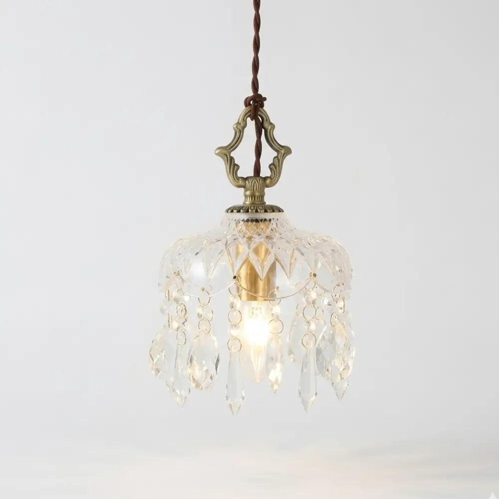 Visão frontal da luminária pendente pequena de 15cm Marquise Radiantbr acesa, com cúpula de vidro facetado tipo cristal e base dourada, em fundo branco.