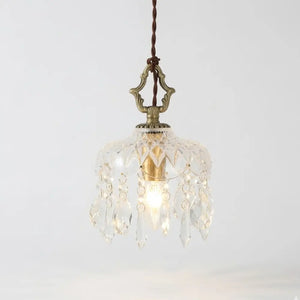Visão frontal da luminária pendente pequena de 15cm Marquise Radiantbr acesa, com cúpula de vidro facetado tipo cristal e base dourada, em fundo branco.