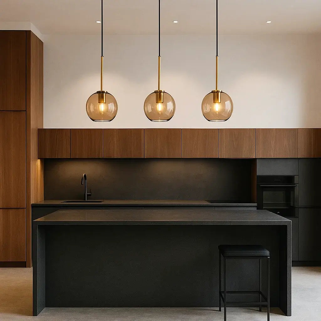 Trio de luminárias pendentes globo âmbar dourado sobre ilha de cozinha moderna em preto e madeira, design minimalista.